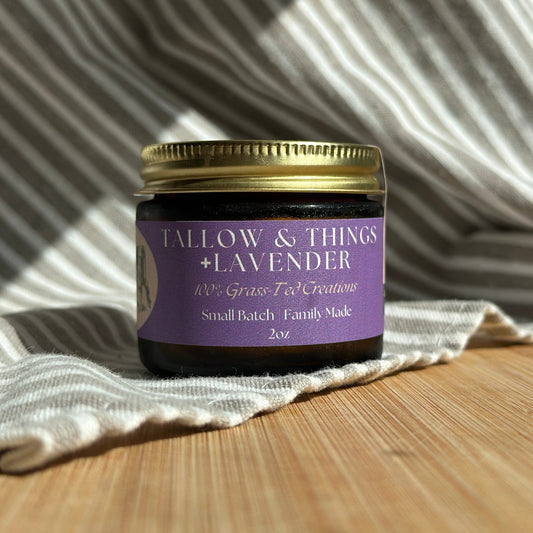 A jar of Tallow & Things Lavender skin tallow balm placed on a wooden surface with a cloth in the background. The label on the jar reads 'Lavender' and indicates the product is a skin balm.